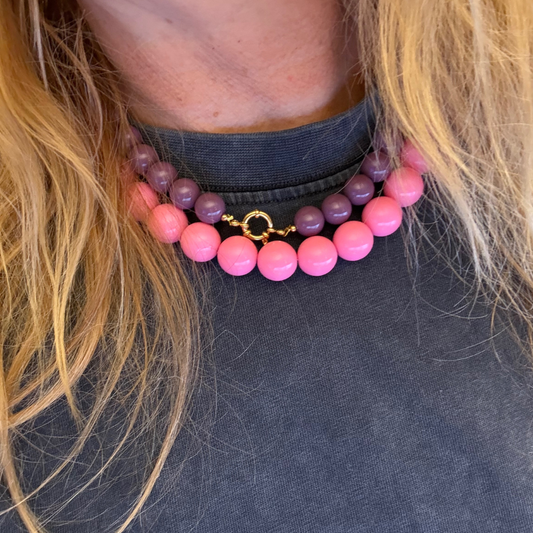 Chunky roze kralenketting met grote glanzende kralen en goudkleurige T-bar sluiting, gedragen op de hals.