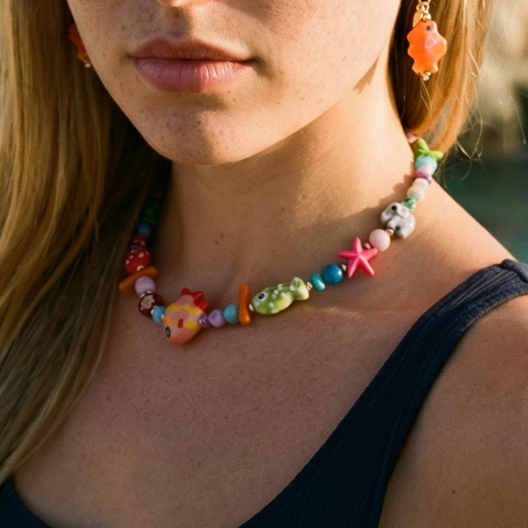 Model draagt kleurrijke kralenketting met vissen en olifanten en oorringetjes met visje.