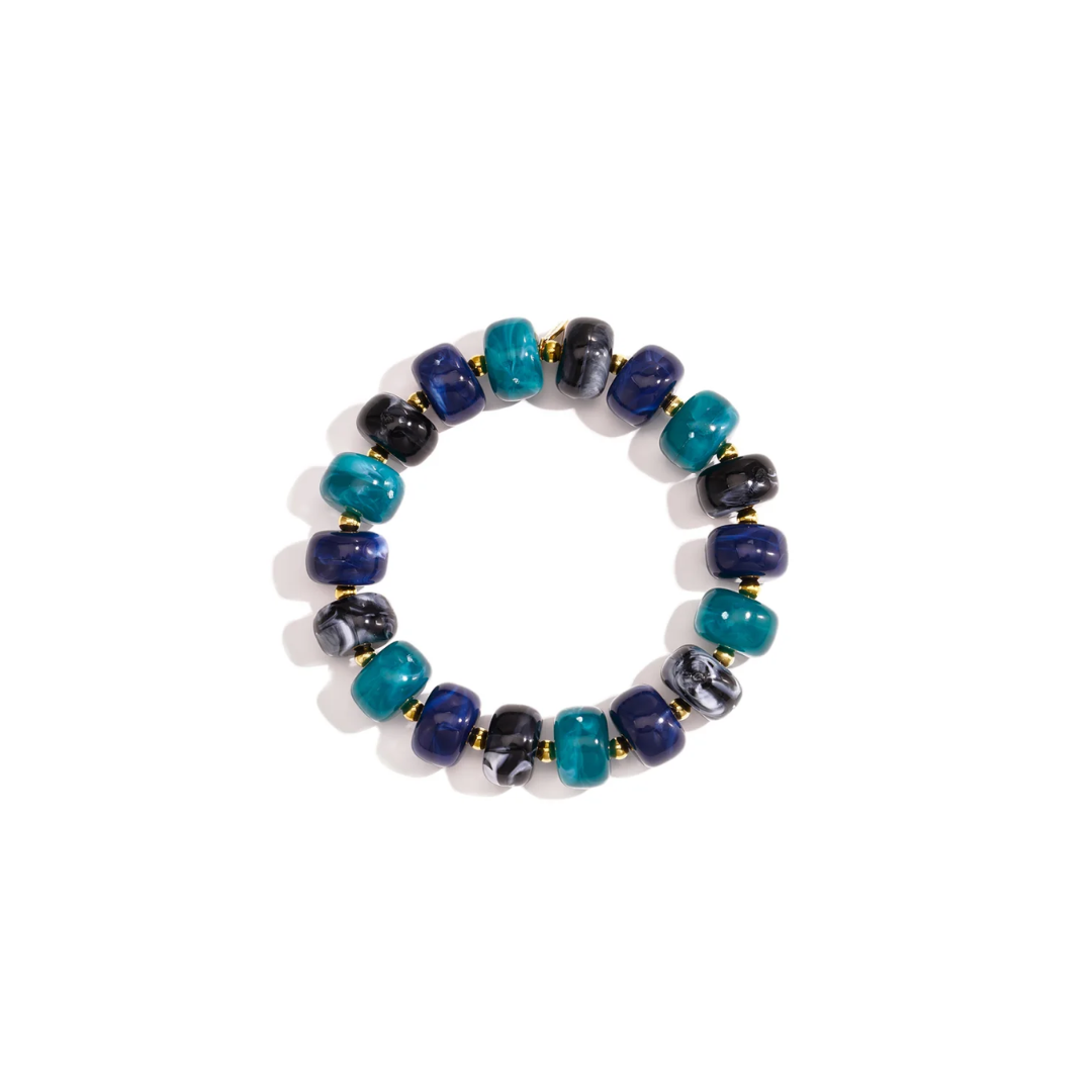 Turquoise blauw chunky kralenarmband Faye met glanzende turquoise, donkerblauwe en zwart gemarmerde kralen en kleine gouden tussenkralen op witte achtergrond.