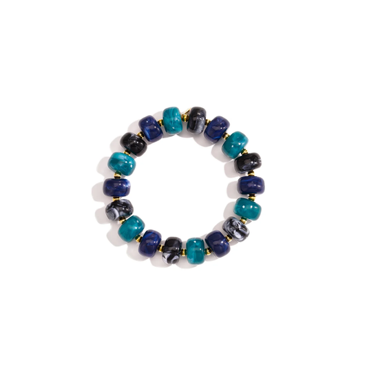 Turquoise blauw chunky kralenarmband Faye met glanzende turquoise, donkerblauwe en zwart gemarmerde kralen en kleine gouden tussenkralen op witte achtergrond.