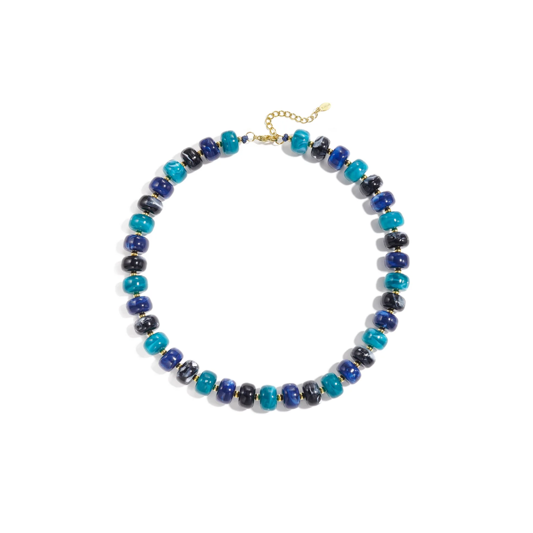 Turquoise blauw chunky kralenketting Faye met glanzende gemarmerde kralen in turquoise, kobaltblauw en donkere blauwtinten, gouden tussenkralen en een verstelbare gouden sluiting op witte achtergrond.