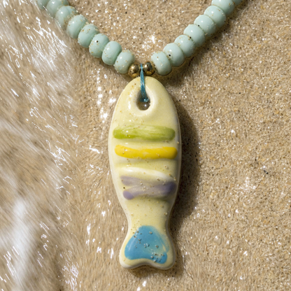 Turquoise kralenketting met keramiek vis bedel van Casa Jadel op het strand
