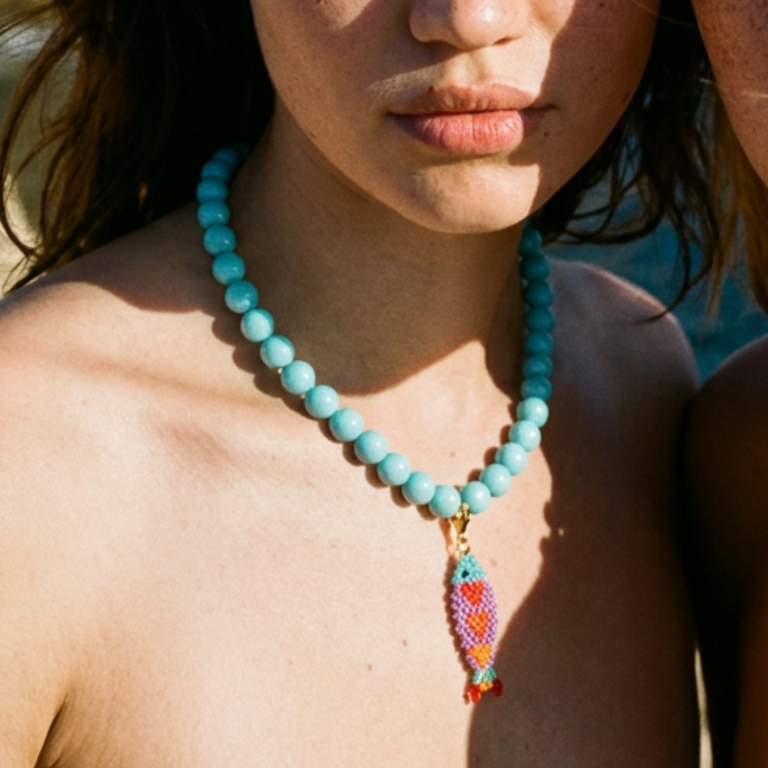 Model draagt turquoise kralenketting met kleurrijke vis bedel van Casa Jadel
