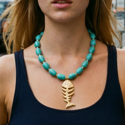 Turquoise kralenketting met ovale kralen en goudkleurige visgraat bedel, gedragen op een donkere top – zomerse statement ketting met Ibiza vibe