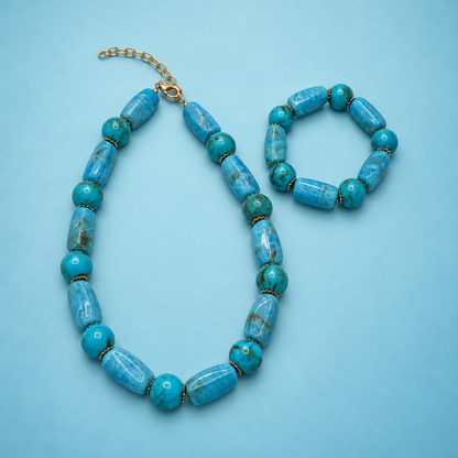 Turquoise long & round marble kralenketting en kralenarmband naast elkaar op een lichtblauwe achtergrond.
