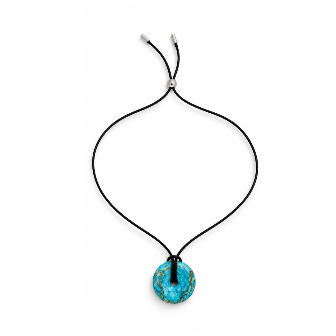 Overzicht van de zwarte koordketting met turquoise ronde statement hanger en zilverkleurige schuifkraal op een witte achtergrond.