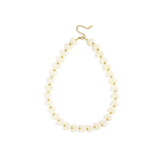Witte hartjes kralenketting met glanzende marmerlook kralen en goudkleurige details, gedragen op een lichte top.