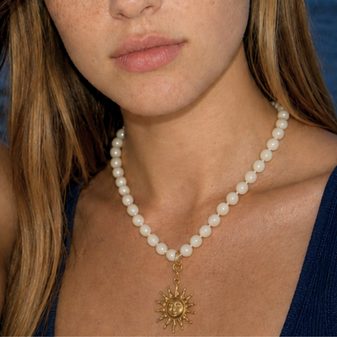 Model draagt een witte kralenketting met goudkleurige zon bedel van Casa Jadel
