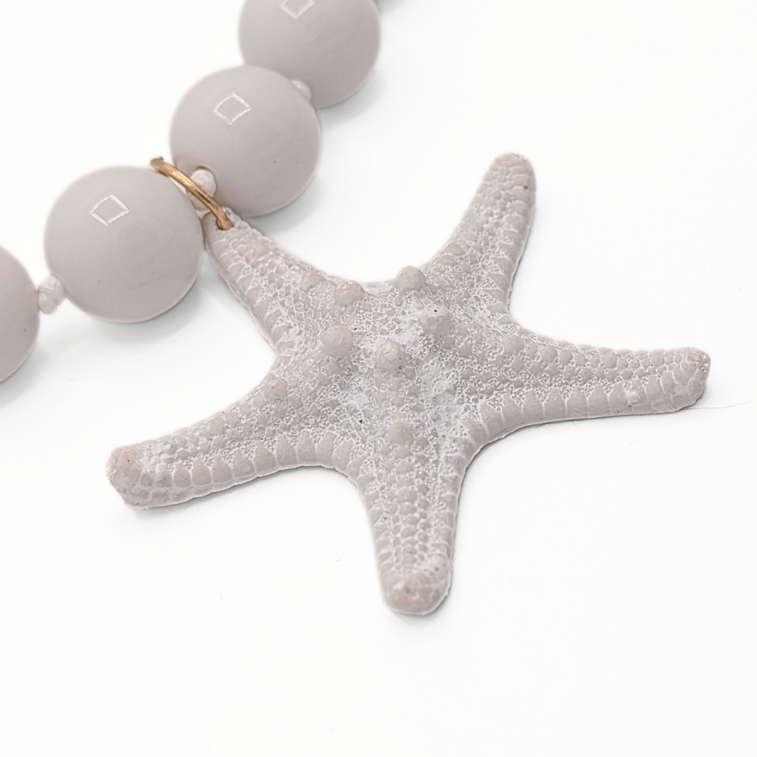 Detail van witte kralenketting met zeesterhanger en glanzende kralen