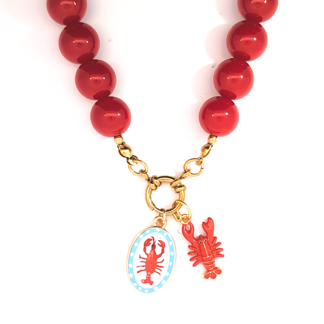 Witte ovale bedel met rode kreeft gedragen aan een kralenketting met goudkleurig boeislot, Jadel.