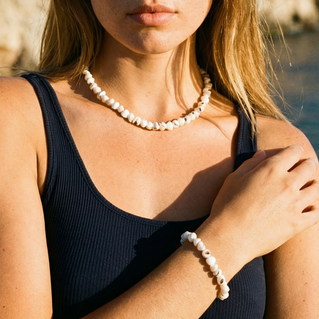 Witte schelpen kralenketting met bijpassende armband, gedragen op een donkere top aan zee – natuurlijke zomerse sieraden met Ibiza vibe