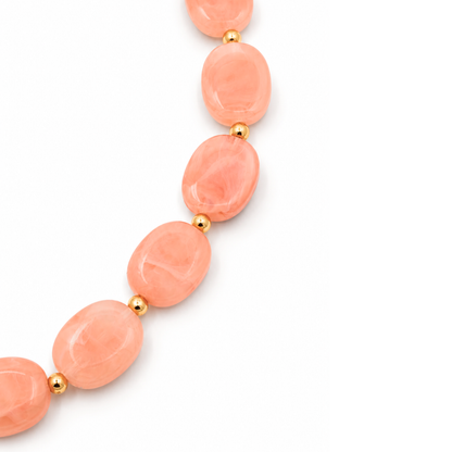 Detail van de platte zalmroze ovale kralen van ketting Gigi met witte marble tekening en kleine goudkleurige tussenkralen.