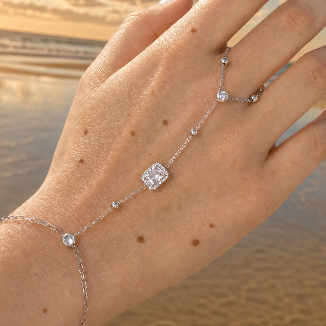 hand met Zilveren hand-chain armband met ring en rechthoekige steen verbonden met fijne schakels
