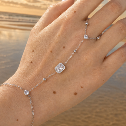 hand met Zilveren hand-chain armband met ring en rechthoekige steen verbonden met fijne schakels