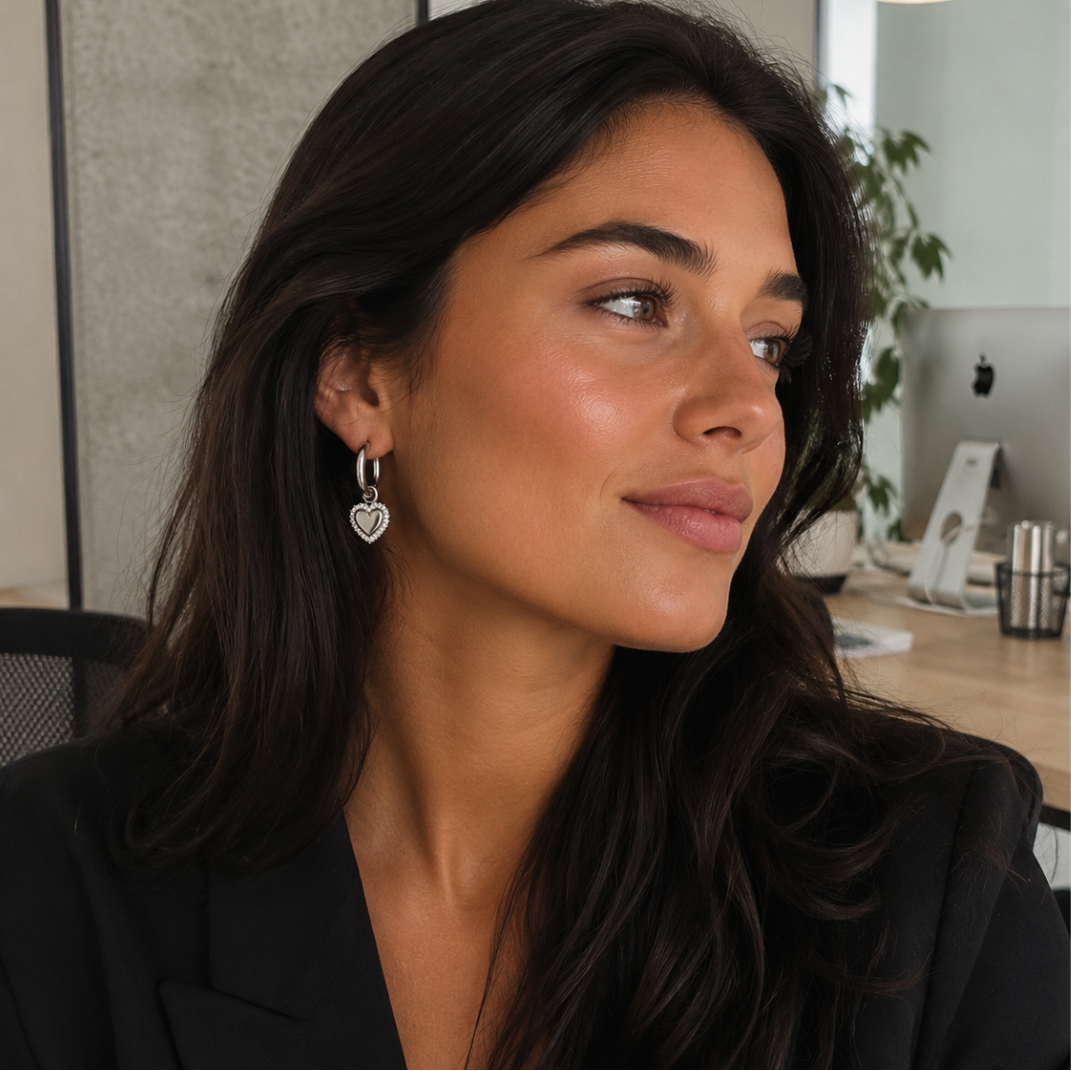 model met Zilveren ovale oorbellen met hartvormige hanger en fonkelende strass steentjes op witte achtergrond