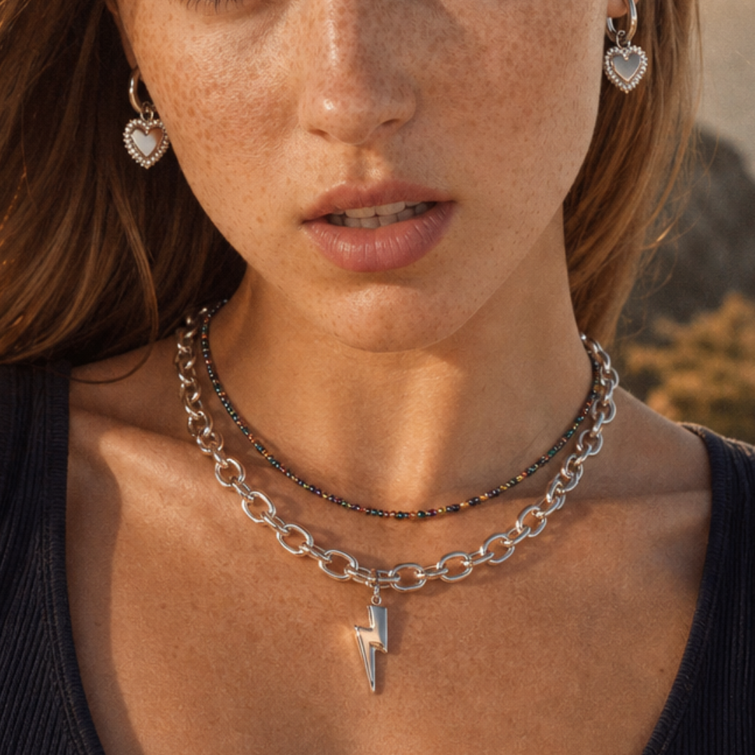 Model draagt een zilveren schakelketting met bliksem bedel, kleurrijke kralenketting en zilveren hart oorbellen van Casa Jadel