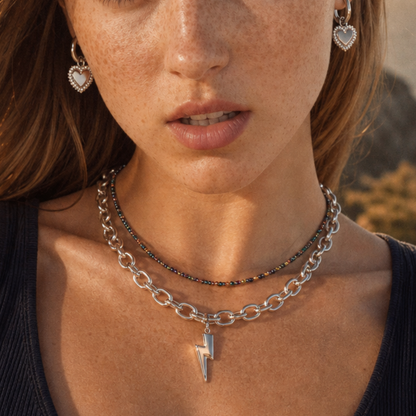 Model draagt een zilveren schakelketting met bliksem bedel, kleurrijke kralenketting en zilveren hart oorbellen van Casa Jadel