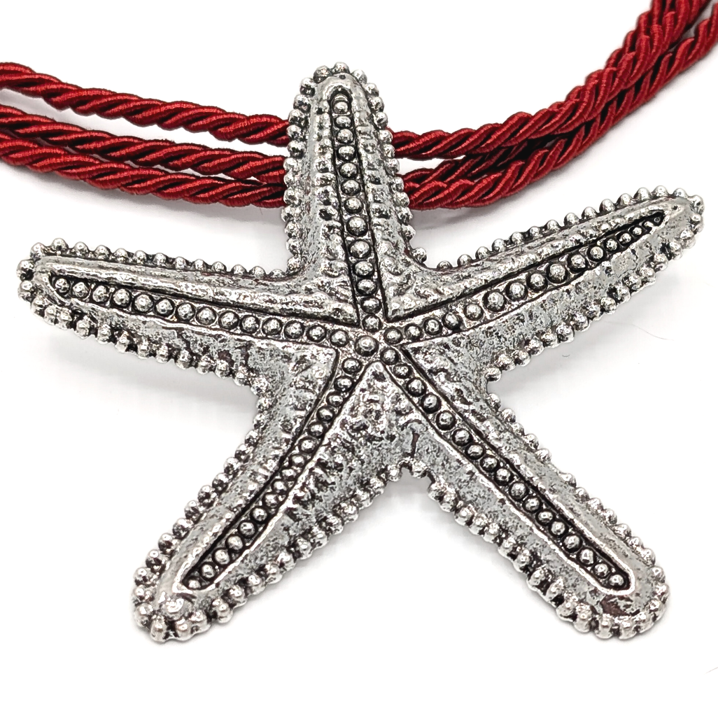 Close-up van grote zilveren zeester hanger aan rode rope ketting