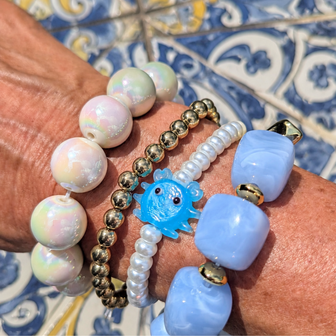 Zomerse armbanden stack met blauwe chunky kralen, parelmoer kralen, gouden kralen en blauw krab bedeltje op een blauw-gele Portugese tegelvloer