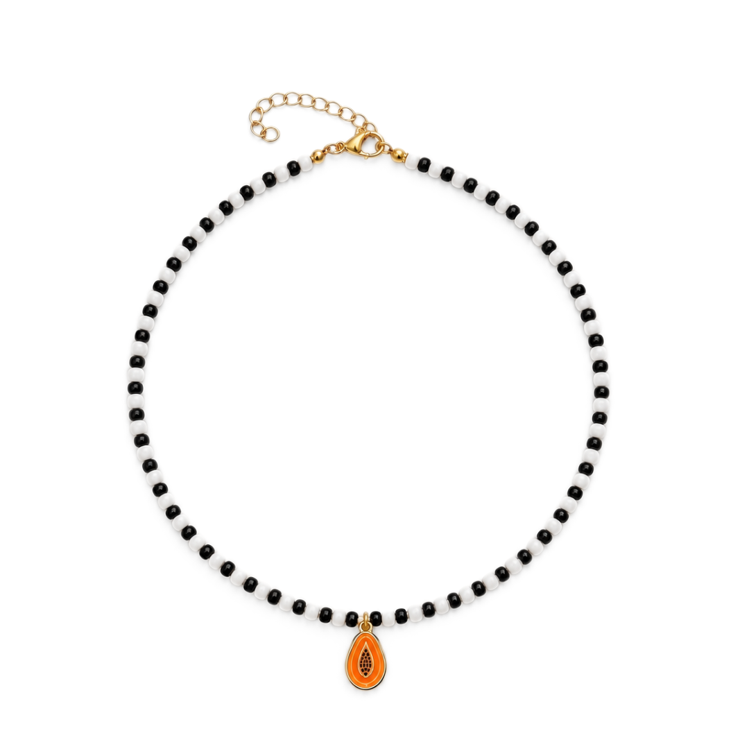 Zwart-witte kralenketting met een oranje papaya bedel met zwarte pitjes, goudkleurige rand en sluiting met verlengkettinkje.