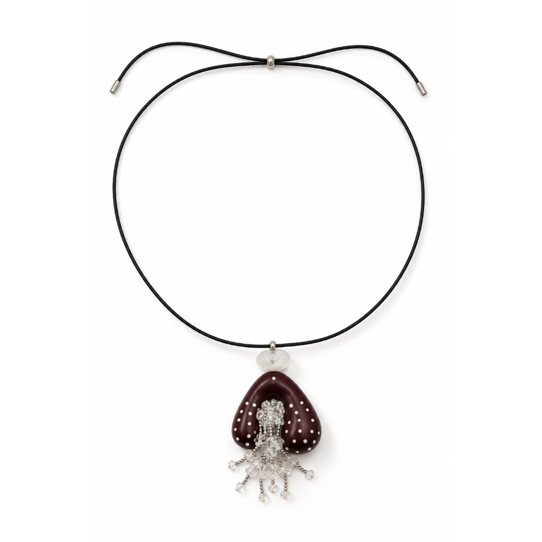 Zwarte lange koordketting met schuifkraal, een wijnrode gestipte hanger en een bergkristal kralen kwastje op een witte achtergrond.