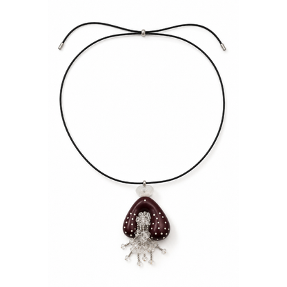 Zwarte lange koordketting met schuifkraal, een wijnrode gestipte hanger en een bergkristal kralen kwastje op een witte achtergrond.