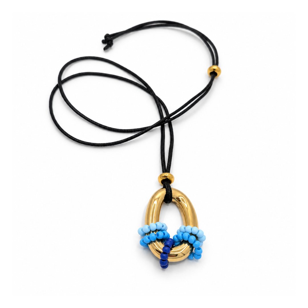 Zwarte lange koordketting met een goudkleurige ovale ringhanger en kleine kralen in lichtblauw, helderblauw en kobaltblauw.