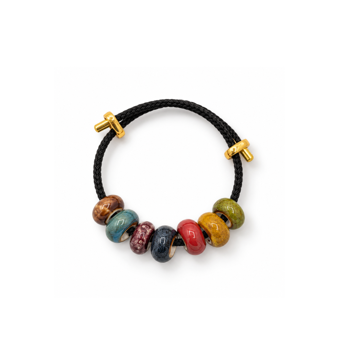 Zwarte gevlochten rope armband met zeven gekleurde keramiek kralen en goudkleurige schuifstukjes op een witte achtergrond.